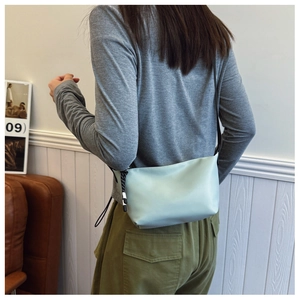 Pale green nylon crossbody dumpling bag worn by model in a cozy living room scene