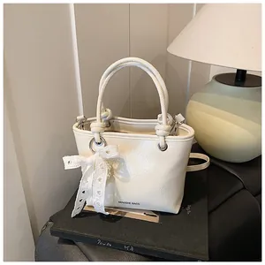 Detail of cream white pleated bucket bag with dual ring handles and lace bow charm