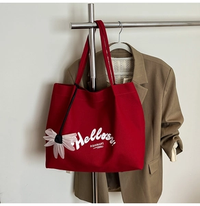 Detail of red canvas tote bag with white lettering and a pink floral mesh charm