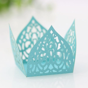 Close-up of light blue laser-cut cupcake wrappers with elegant crown pattern and floral lace