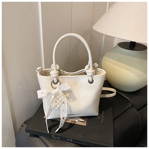 Detail of cream bucket bag featuring delicate lace bow, pearl charm, and logo bottom