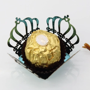 Detail of laser-cut crown hollow paper box with a golden chocolate ball on a white base