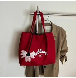 Detail of red canvas tote bag featuring white Hello lettering and floral charm