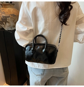 Detail of glossy black Boston bag with dual handles and silver chain shoulder strap