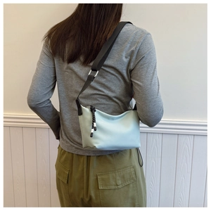 Close-up of mint blue nylon dumpling bag with black strap and decorative woven zipper pull