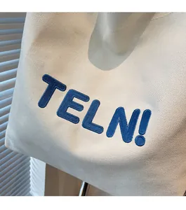 Dettaglio del ricamo blu sulla trama della borsa tote in tela robusta bianco avorio