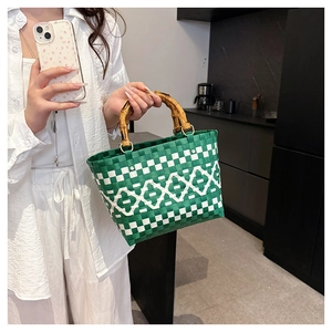 Détail d'un sac seau tressé vert et blanc avec des poignées en bambou naturel