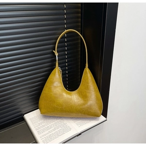 Detail view of mustard yellow crescent shoulder bag with crocodile texture on a book
