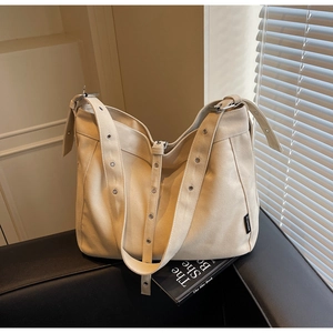 Detail of beige canvas tote bag showing metal eyelets and side woven brand tag
