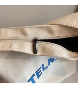 Dettaglio della cerniera in metallo e ricamo blu sulla borsa tote in tela beige