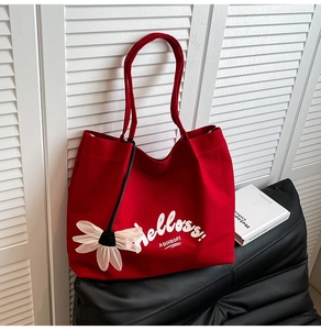 Detail shot of a large red canvas tote bag with white floral pendant on a dark sofa