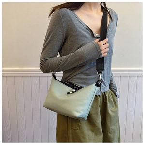 Detail of mint green crossbody dumpling bag with wide black strap and text ribbon