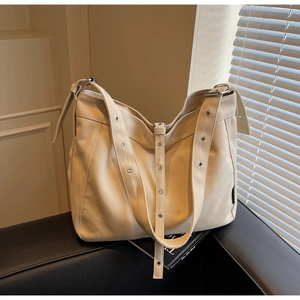Detail of beige canvas tote bag with adjustable metal eyelet strap on a book props background