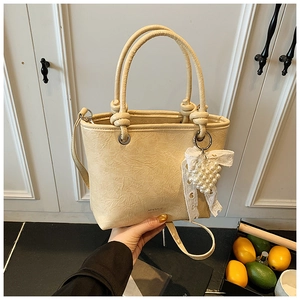 Detail of beige pleated tote bag with knotted handles and a delicate lace pearl charm