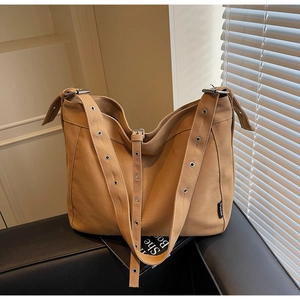 Close-up of camel canvas tote bag showing wide shoulder strap with metal eyelet detail