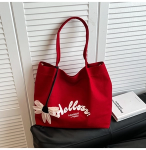 Detail of red canvas tote bag with white floral pendant and artistic lettering