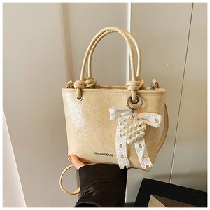 Detail of cream pleated crossbody bag with lace bow and pearl heart charm accessory