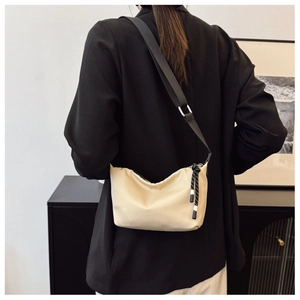 Beige crescent bag with black wide strap shown on shoulder against a black blazer