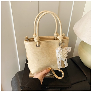 Detail of cream pleated bucket bag featuring pearl lace bow charm and brand logo