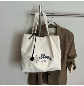 Detail of canvas tote bag with black strap and white floral charm on a hanger