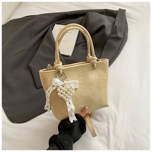 Detail of beige pleated bucket bag with pearl heart charm and lace bow decoration