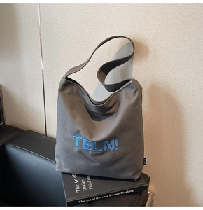 Dettaglio della borsa tote in tela grigio scuro con ricamo TELN blu e tracolla larga