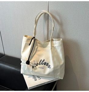 Close-up of off-white canvas tote bag with floral pendant on a black leather sofa