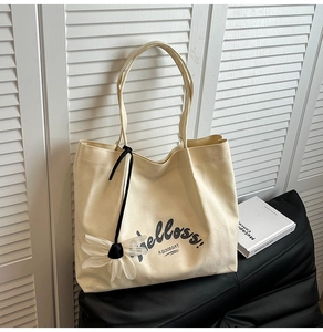 Close-up of beige canvas tote with Helloss print and white daisy flower charm detail