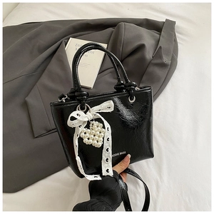Detail of black glossy wrinkled PU leather with pearl heart charm and lace bow