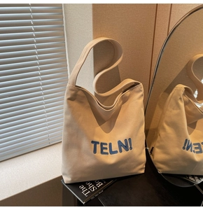 Dettaglio della borsa tote in tela crema con ricamo TELN blu e luce naturale soffusa