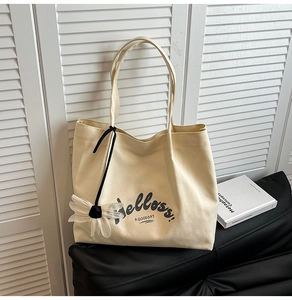 Detail of canvas tote bag featuring black typography and white floral charm accessory