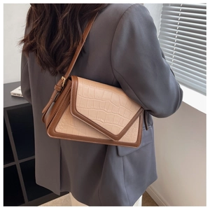 Detail of beige faux crocodile leather shoulder bag with brown trim and metal buckle
