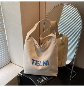 Dettaglio della borsa tote in tela beige con ricamo TELN blu su un tavolo minimalista