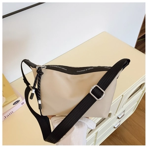Detail of beige nylon dumpling bag featuring adjustable black strap and logo zipper