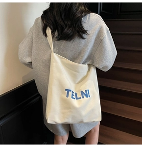 Dettaglio della borsa tote in tela bianca con ricamo TELN blu indossata da una modella