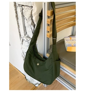 Détail du sac demi-lune vert foncé avec poche latérale et sangle sur une chaise en bois