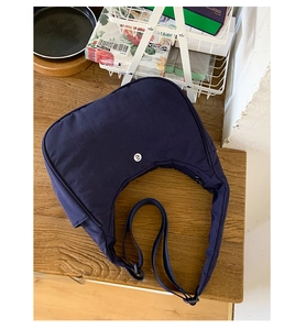 Vue de dessus d'un sac bandoulière en nylon bleu foncé en forme de croissant sur une table en bois