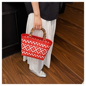 Détail du sac seau tressé rouge et blanc avec anses en bambou et texture à carreaux