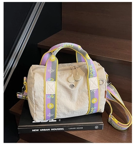 Dettaglio borsa Boston beige con tracolle colorate con lettere su un libro