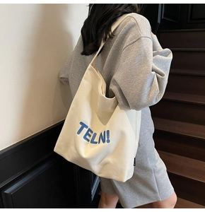 Dettaglio della borsa tote in tela crema con ricamo blu indossata da un modello