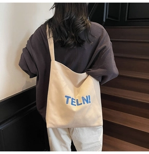Modella indossa borsa tote in tela crema con ricamo blu su una scala in legno