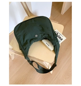 Détail d'un sac demi-lune en nylon vert foncé avec petit logo métallique sur bois