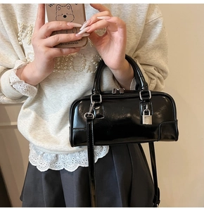 Detail of glossy black Boston handbag featuring a silver lock and detachable strap