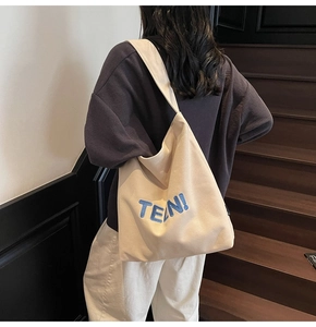 Dettaglio della borsa tote in tela bianca con ricamo blu TEN indossata dal modello