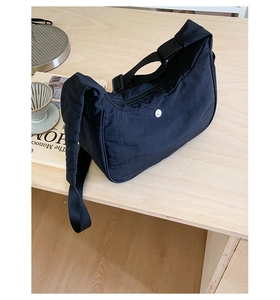 Détail du sac croissant en nylon noir avec bandoulière réglable et petit logo blanc
