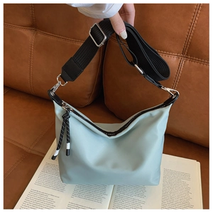 Detail of mint green nylon crossbody bag with black adjustable strap and woven zipper pull
