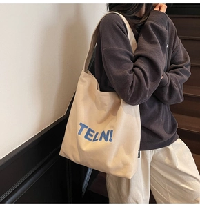 Dettaglio della borsa tote in tela beige con ricamo TELN! blu e tracolla per la spalla