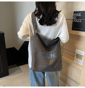 Dettaglio della borsa tote grande in tela marrone con ricamo blu indossata da una modella