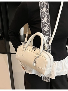 Fashionable beige Boston handbag with crossbody strap shown on a black outfit
