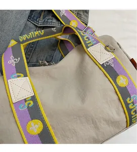 Dettaglio borsa in nylon beige con tracolla a righe colorate e logo in metallo lucido
